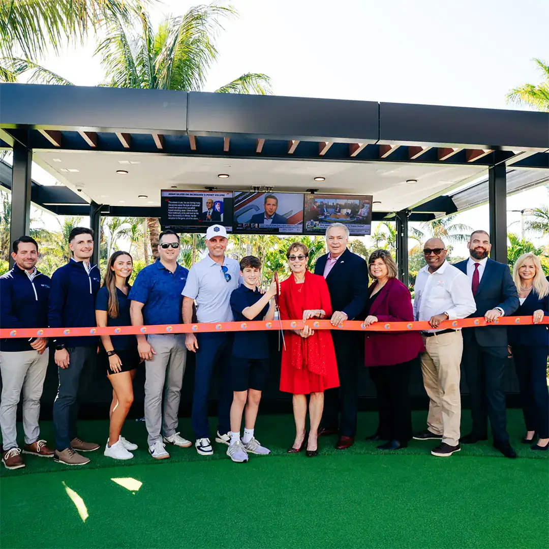 Group of people stands together, smiling, in front of a large ribbon.