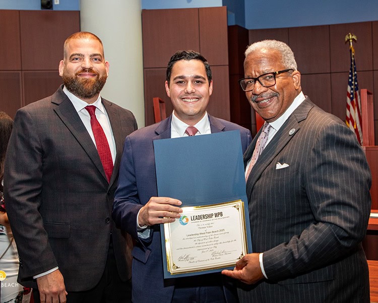 Three men in suits, one holding a framed leadership award certificate, smiling at the camera.