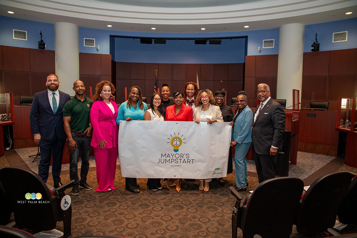 Group of diverse people holding a Mayor's Jumpstart banner in a courtroom.