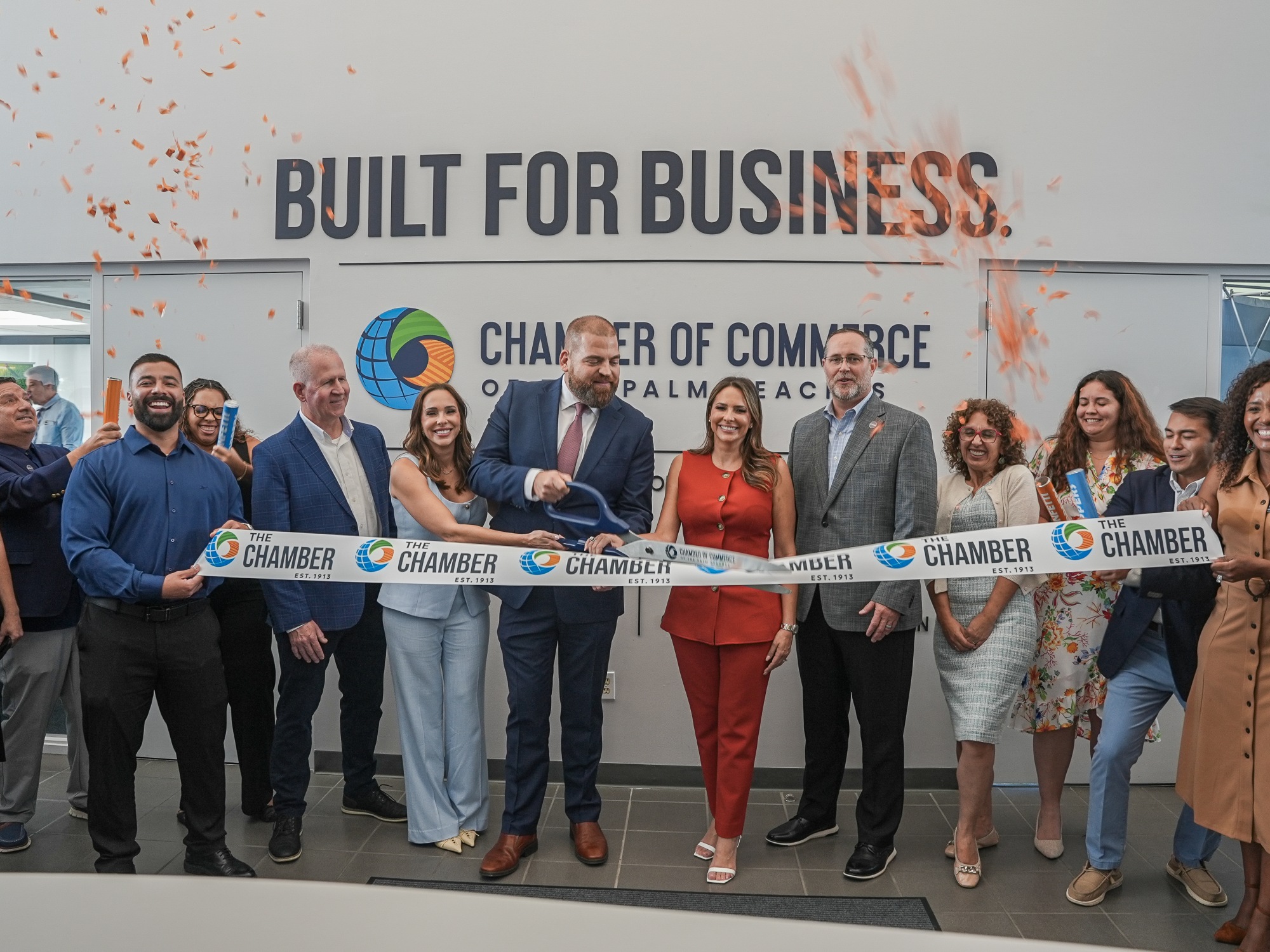 Group of diverse people at ribbon-cutting ceremony in front of business sign.