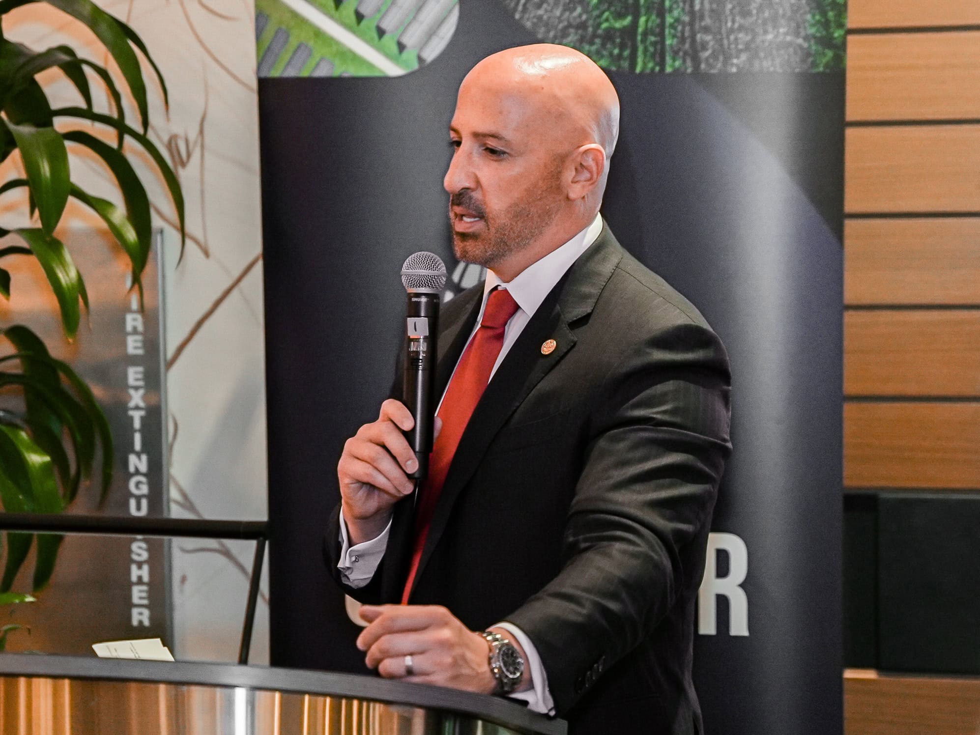Bald man in a suit speaking into a microphone at a professional event.