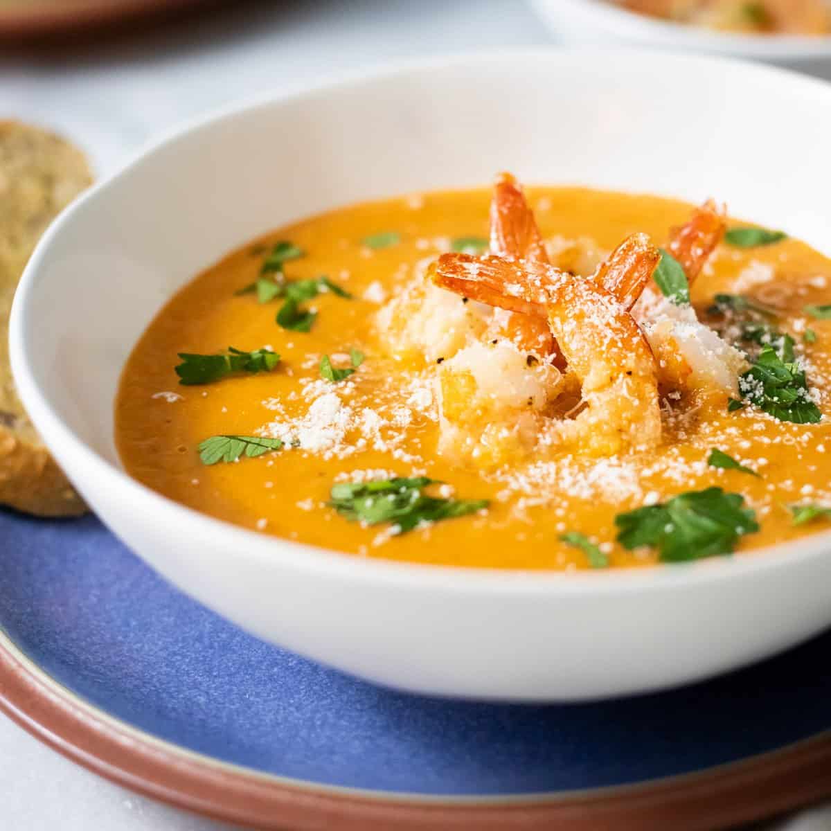 roasted tomato soup in a bowl topped with shrimp, parsley, and parmesan cheese