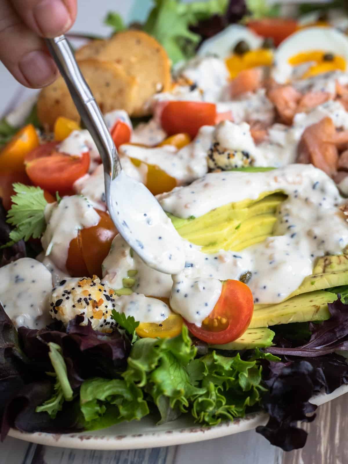 Everything bagel yogurt dressing being drizzled on everything cobb salad with smoked salmon.
