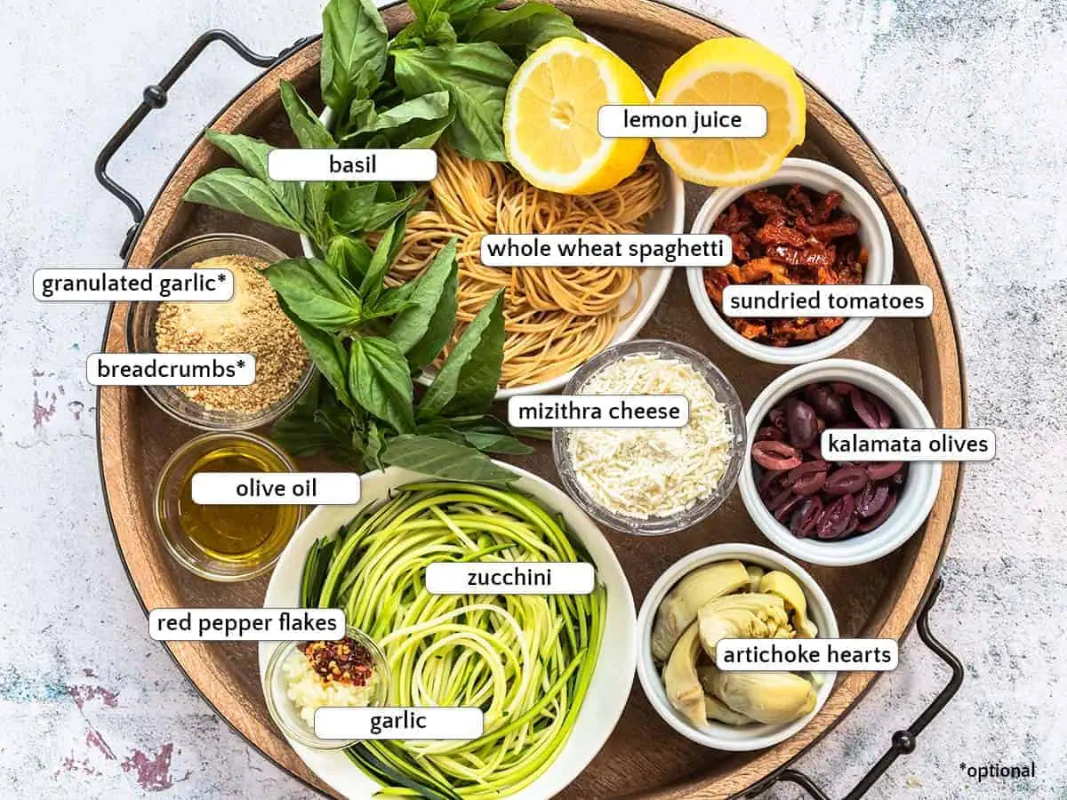 Ingredients for Mediterranean zucchini spaghetti include zucchini noodles, whole wheat pasta, kalamata olives, sundried tomato, artichoke hearts, olive oil, red pepper flakes, garlic, garlic powder, breadcrumbs, lemon juice, basil, and mizithra cheese.