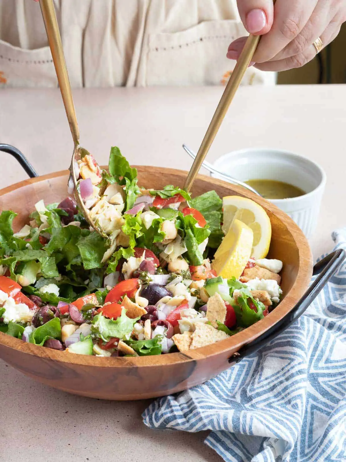 Loaded Greek Salad being tossed with dressing in a bowl with salad servers.
