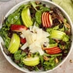 Apple and asiago salad in a bowl, featuring crisp salad greens, sliced red and green apples, shaved asiago cheese, toasted walnuts, and tart dried cranberries. It is dressed with an easy maple-Dijon vinaigrette.