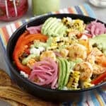 Shrimp and avocado salad in a bowl accompanied by a jar of cilantro avocado dressing and pickled onions.