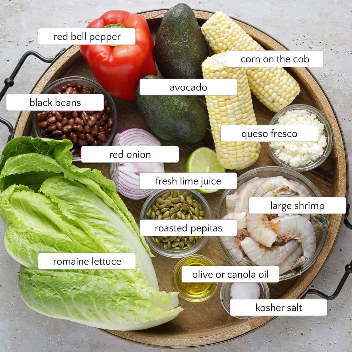 Shrimp and avocado salad ingredients include large shrimp, avocado, corn, queso fresco, kosher salt, olive oil, roasted pepitas, fresh lime juice, red onion, romaine lettuce, black beans, and red bell pepper.