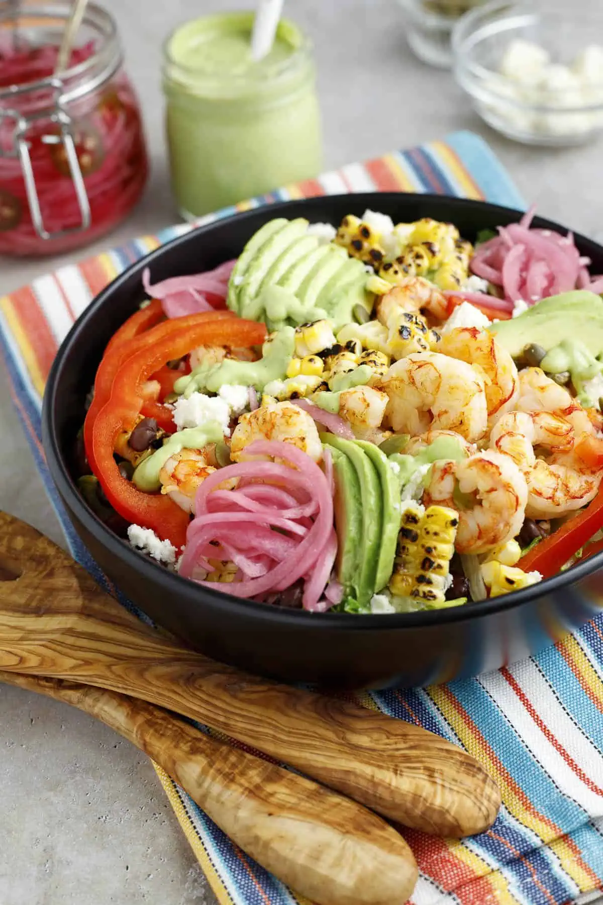 Shrimp and avocado salad is shown in a bowl dressed with cilantro avocado dressing. Salad tossers sit next to the bowl.