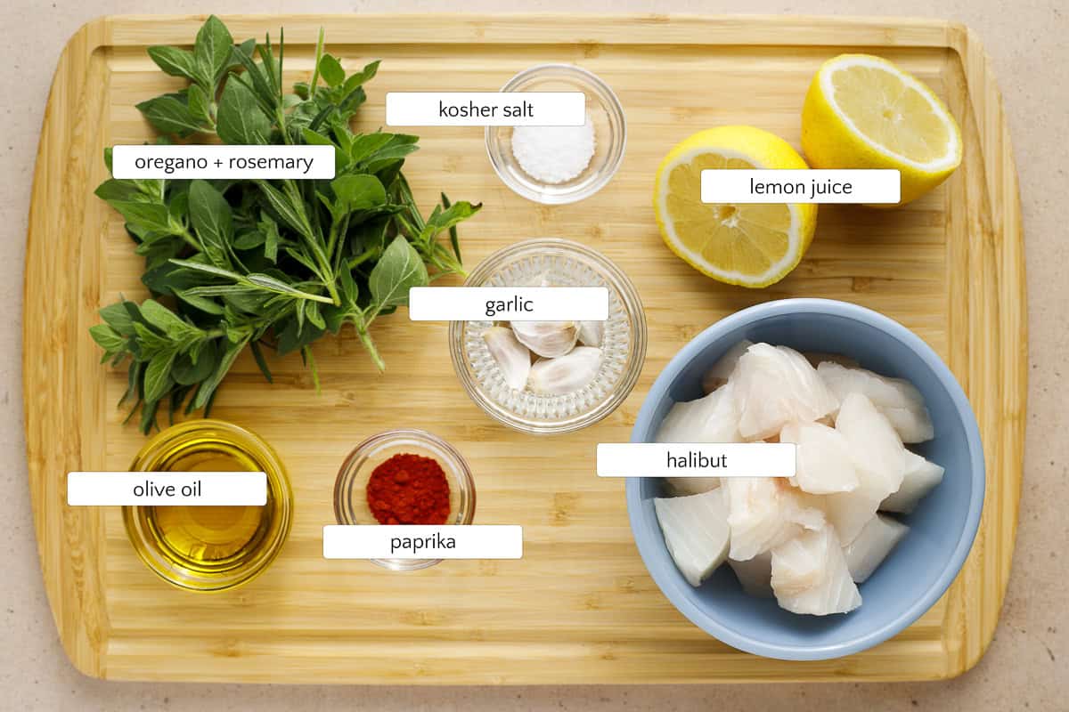 Ingredients for grilled halibut skewers include fresh oregano and rosemary (dried will work), fresh lemon juice, salt, olive oil, paprika, garlic, and halibut.