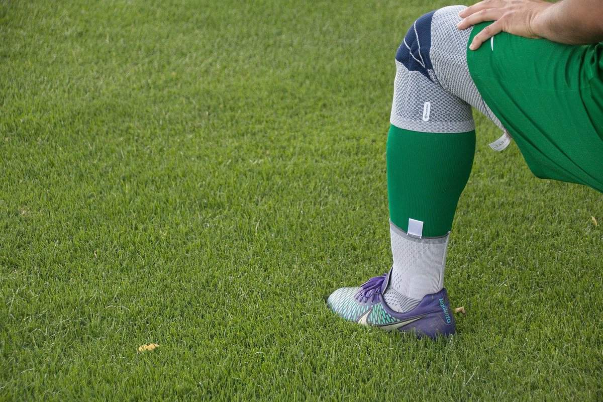 Athletic person's knee brace on grass during stretching exercise.