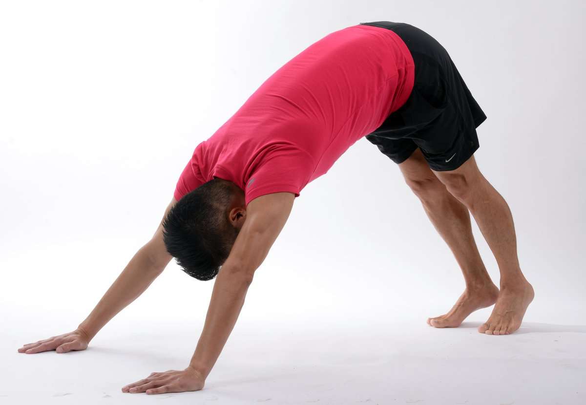 Flexible young man performing yoga stretch in studio with white background.