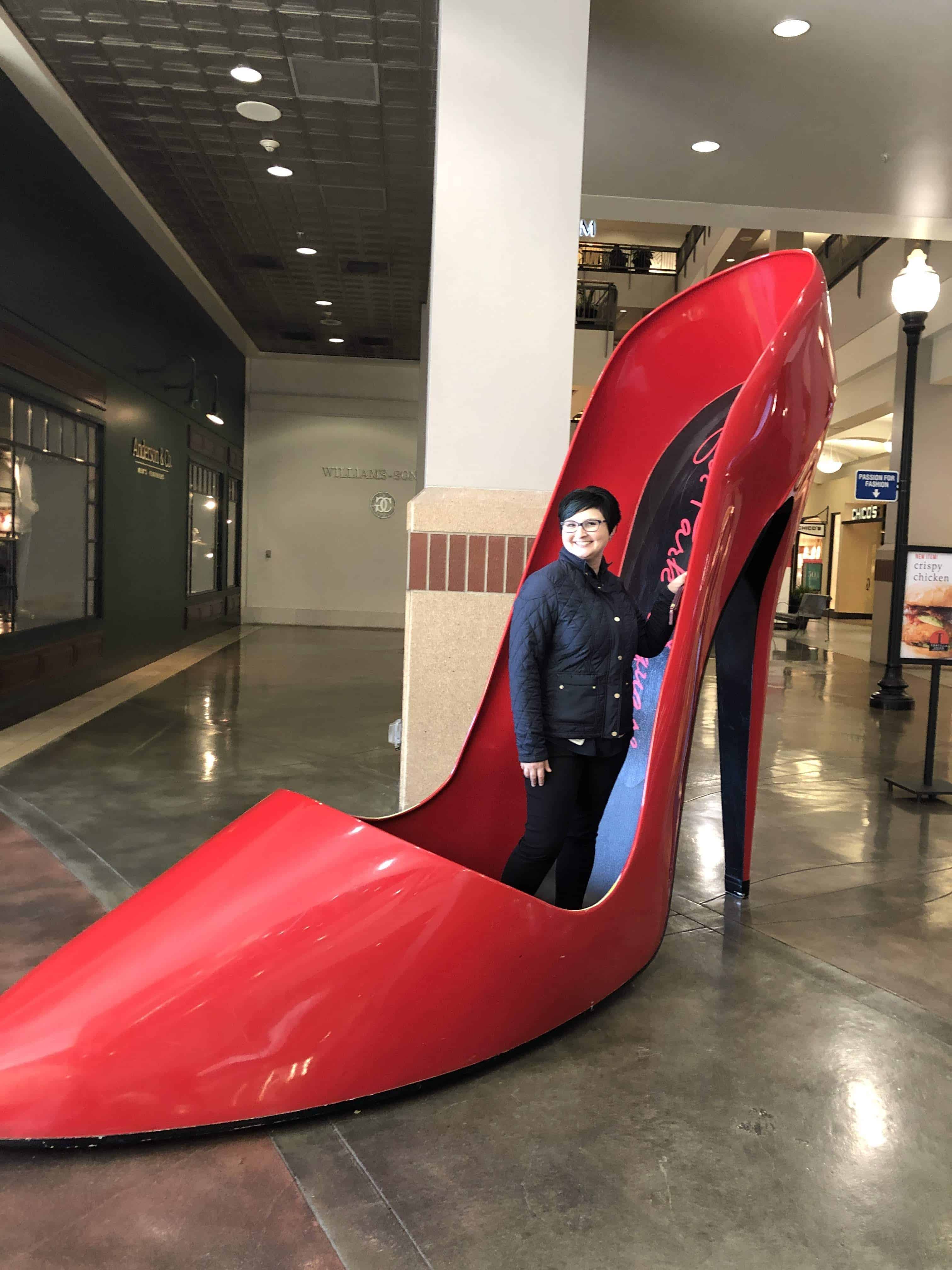 Amy standing in a big red shoe in the mall in Spokane