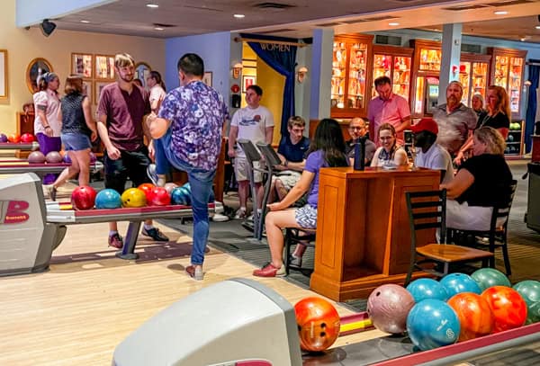 A group of people socializing around the bowling ball return machines at a bowling alley. Colorful bowling balls sit in the machines.