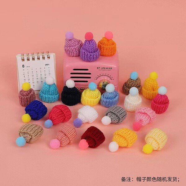 Cute knitted hats with multicolored pom-poms for kids, displayed on a pink background.