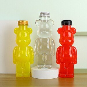 Bright yellow, clear, and red bear-shaped bottles for beverages, displayed on a wooden surface with.