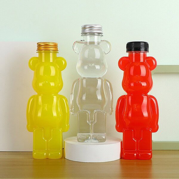 Bright yellow, clear, and red bear-shaped bottles for beverages, displayed on a wooden surface with.