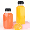 Clear plastic bottles with yellow and orange liquids, lemon slice, on pink block.
