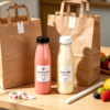 Custom plastic bottles for juice and milk with paper bags on a wooden table.