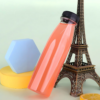 Clear plastic juice bottle with black cap next to Eiffel Tower model and geometric decor.