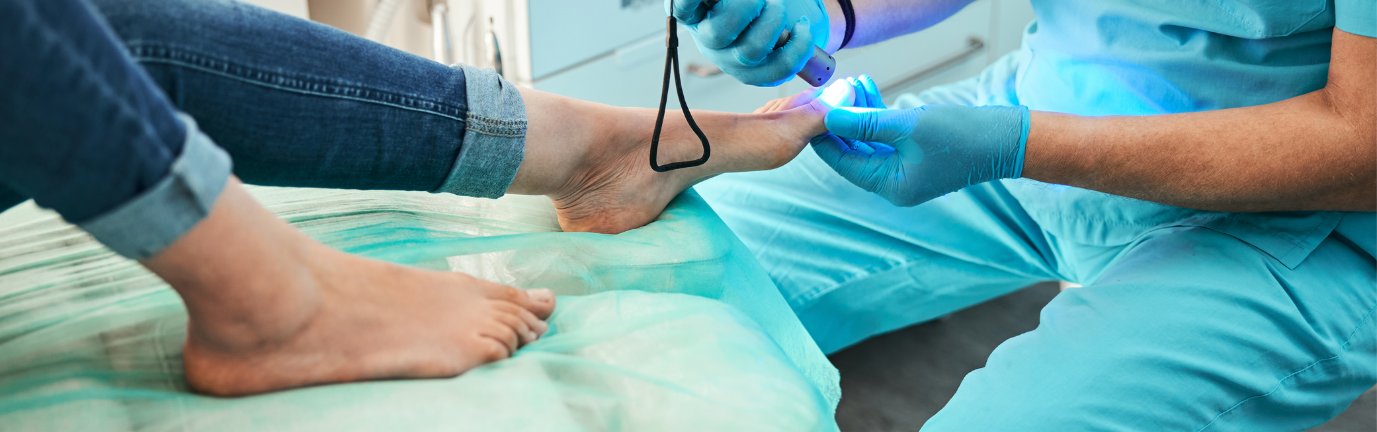 Trattamento podologico con medico che utilizza strumenti e luce blu su piede di paziente