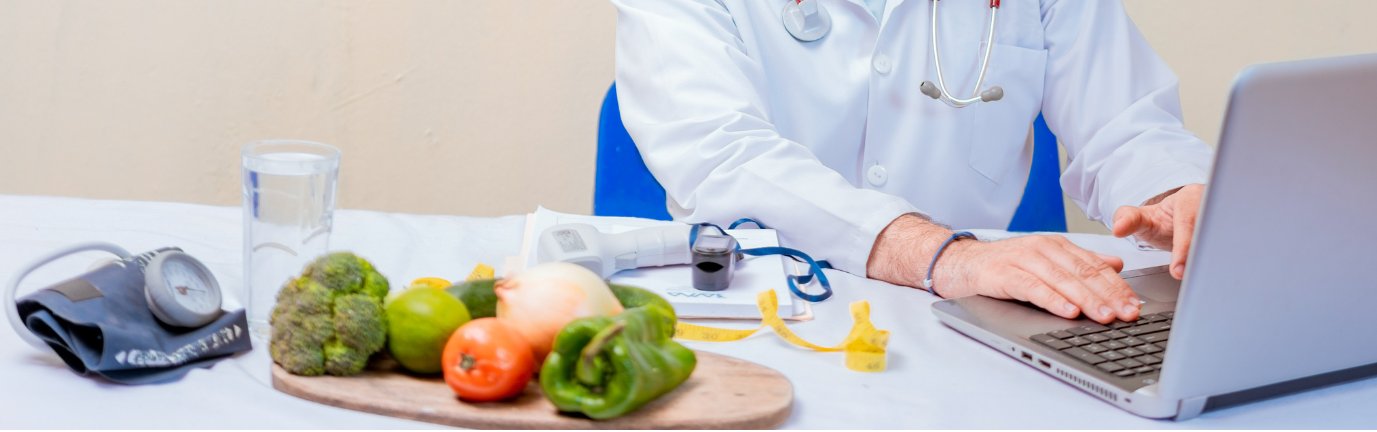 Medico dietologo lavora al computer con strumenti medici e alimenti sani sul tavolo durante una visita dietologica