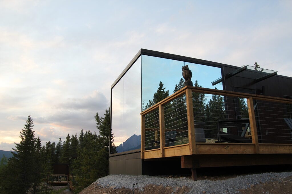 Contemporary glass-front mountain cabin with a wooden balcony and forest views.