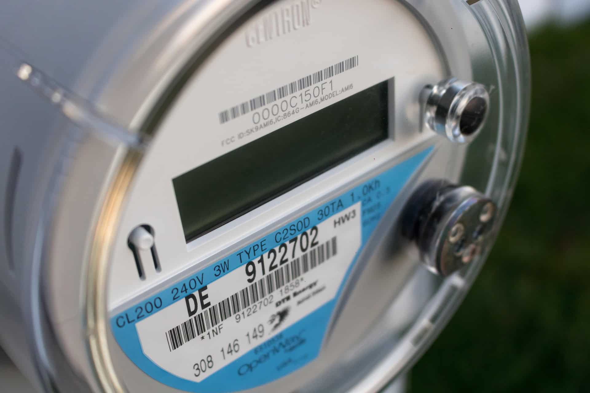 Gros plan sur un compteur électrique intelligent moderne, montrant un écran numérique, des codes-barres et des numéros d'identification sur son boîtier argenté.