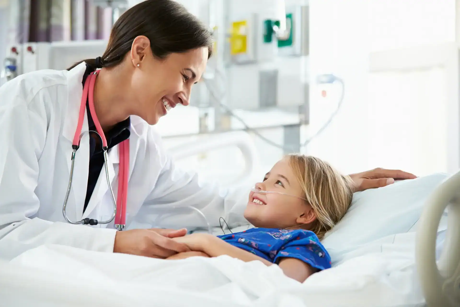 Doctor smiling at young patient in hospital bed during check-up.