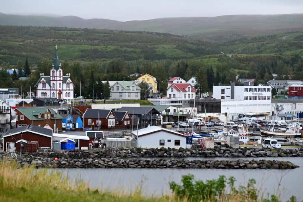 Scenic view of Húsavík harbor with colorful buildings and boats, leading to the iconic Hvitserkur ro.