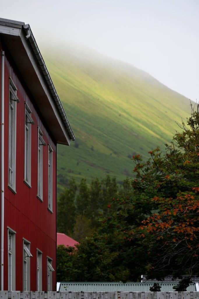 Scenic view of a red house with lush green mountains in the background, shrouded in mist, during a c.