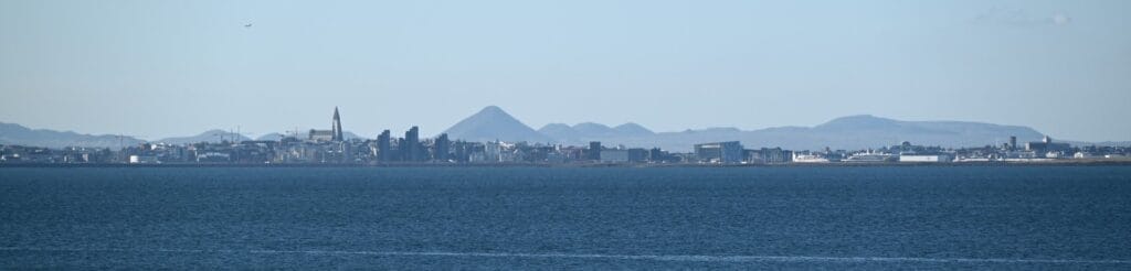 Scenic view of Reykjavík city skyline from Hvalfjörður fjord, showcasing mountains and urban landsca.
