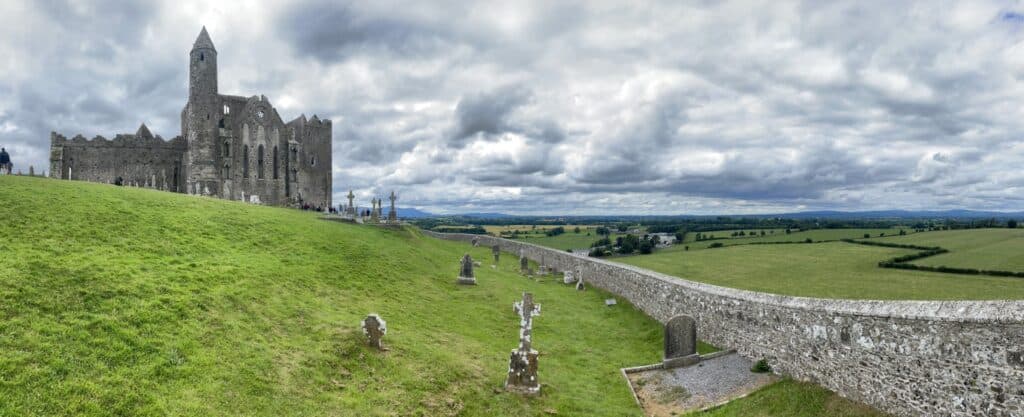 Ancient Irish castle atop a lush green hill with a stone wall, under a cloudy sky, part of the Dubli.