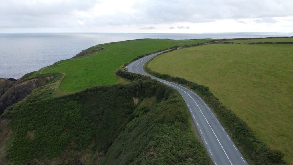 A winding coastal road with lush green hills near the ocean in Ireland.