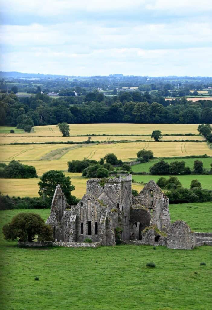 Ancient stone ruins set in lush green fields, with rolling countryside in the background.