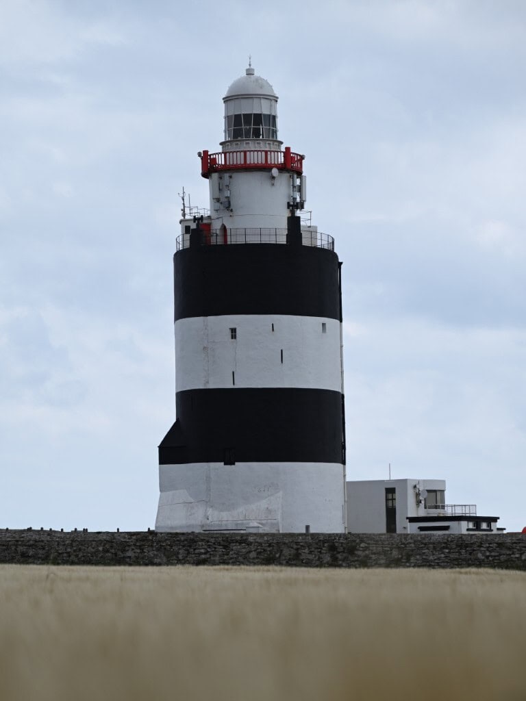 Lighthouse on the Irish Copper Coast with rugged coastline and cloudy sky in the background.