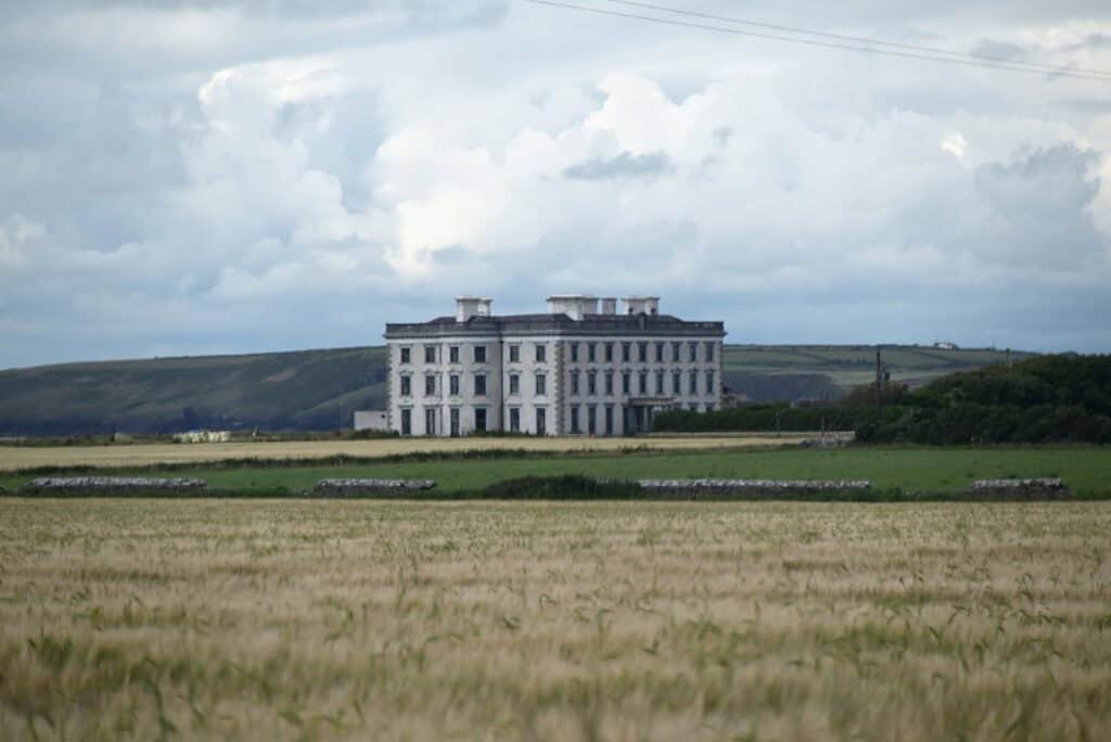 Irish castle overlooking lush green fields on the Copper Coast, Cork, with dramatic cloudy sky.