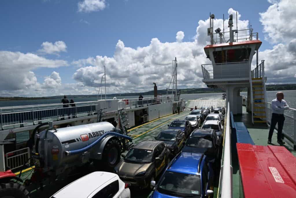 Ferry deck with cars traveling from Dingle to Dublin under a partly cloudy sky.