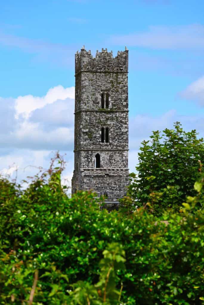 Ancient stone tower surrounded by lush greenery in Ireland.