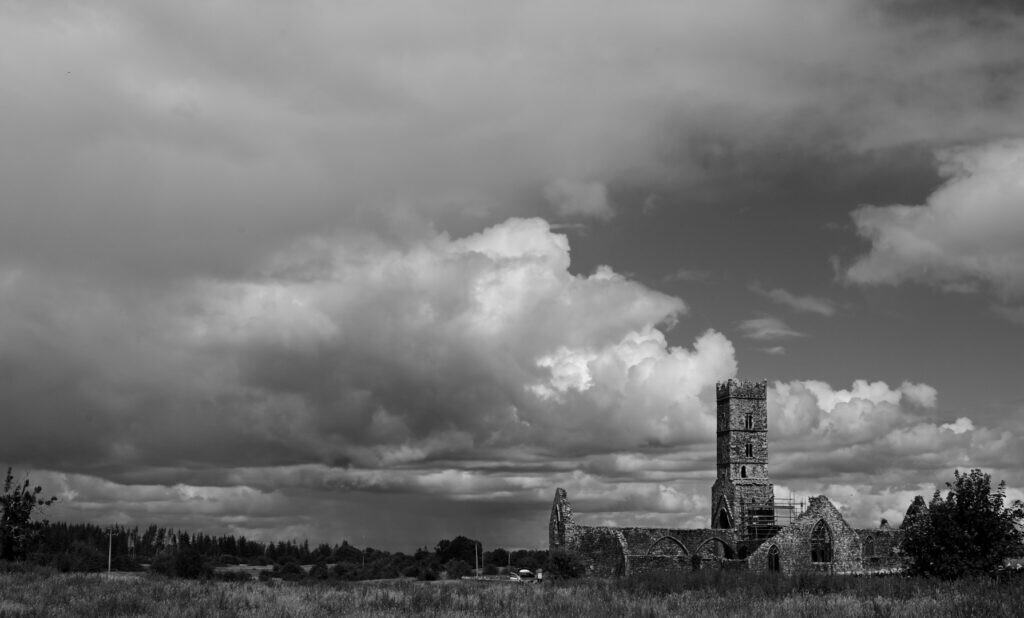 Ancient church ruins near Dingle, Ireland, under dramatic cloud-filled sky.