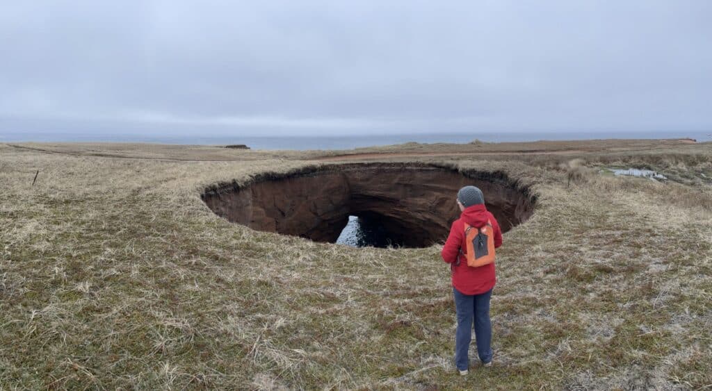 Person observing a large natural hole in the landscape of Îles-de-la-Madeleine in May.