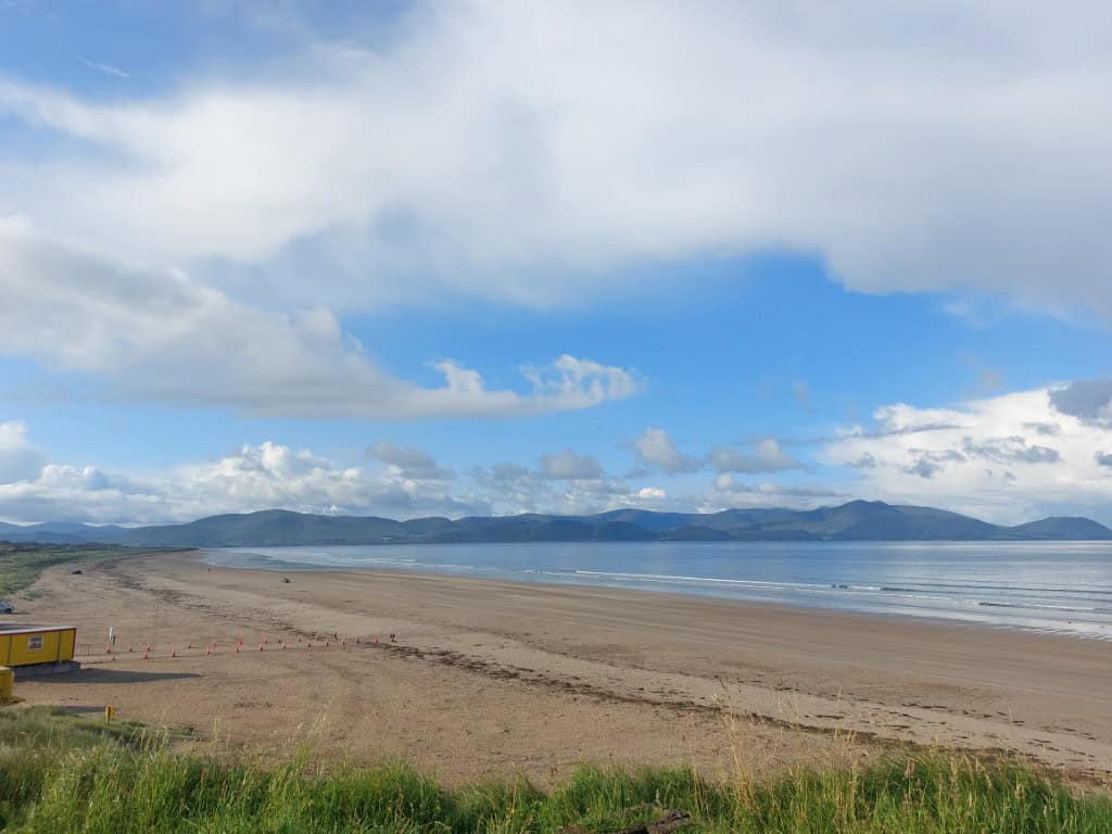 Scenic view of Dingle Peninsula coastline with sandy beach and blue sky.