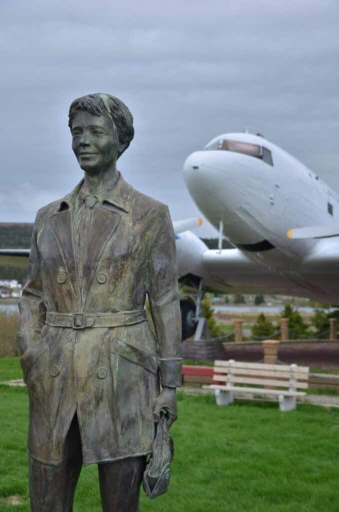 Bronze statue of a woman at Harbour Grace Airfield, with a vintage aircraft in the background.