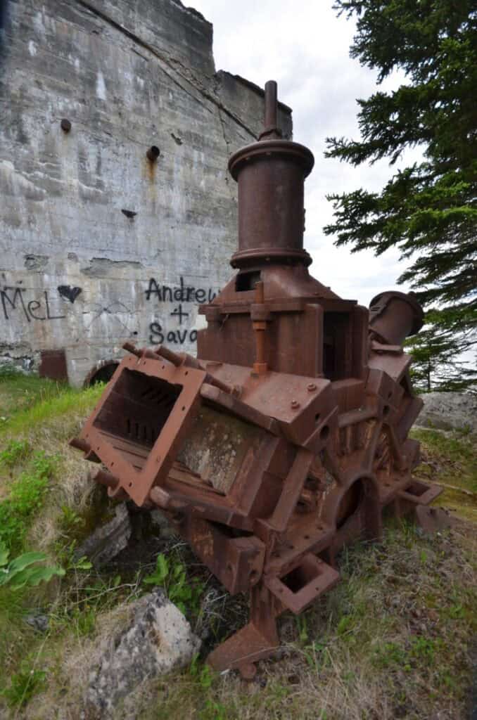 Old, abandoned metal equipment with weathered surface and overgrown surroundings.