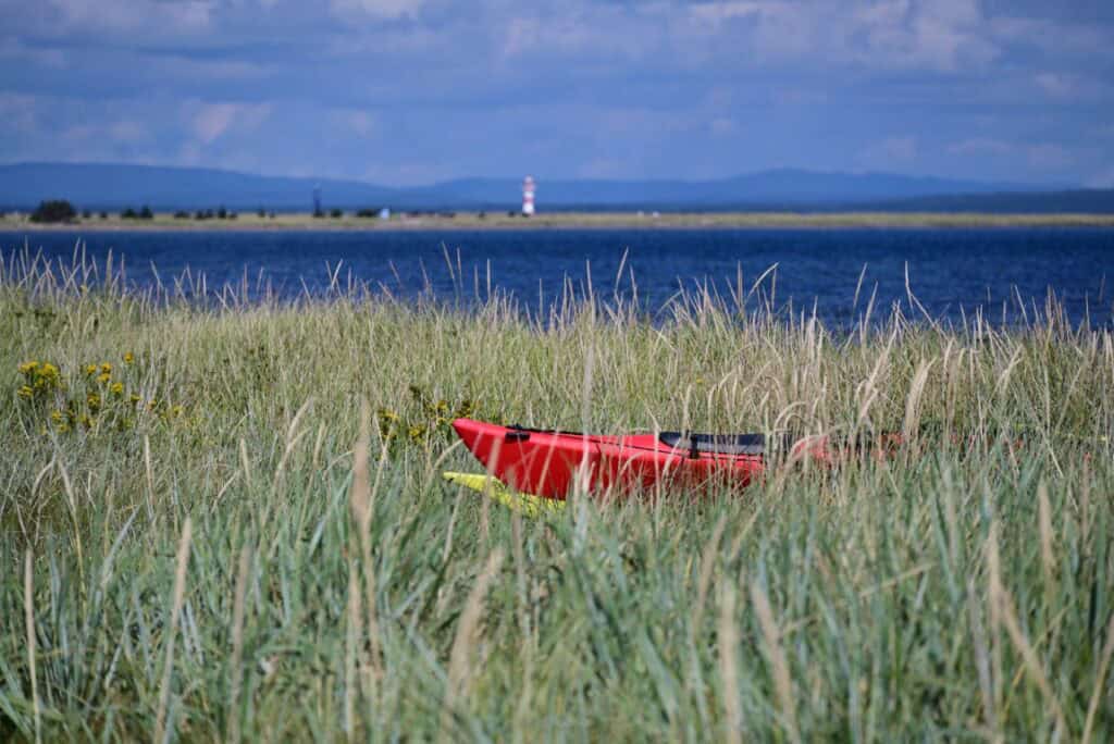 Kayak resting on grassy shoreline at Sandy Point with water and lighthouse in background.