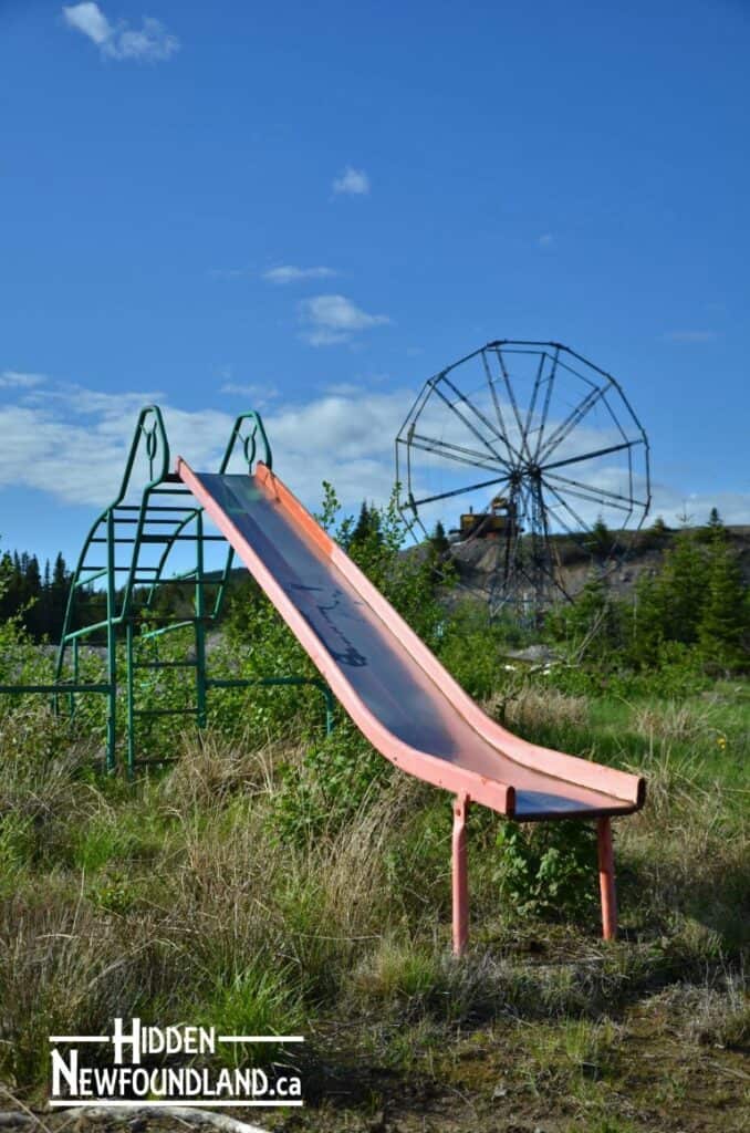 Abandoned playground slide and Ferris wheel at The Trinity Train Loop, Newfoundland, showcasing scen.
