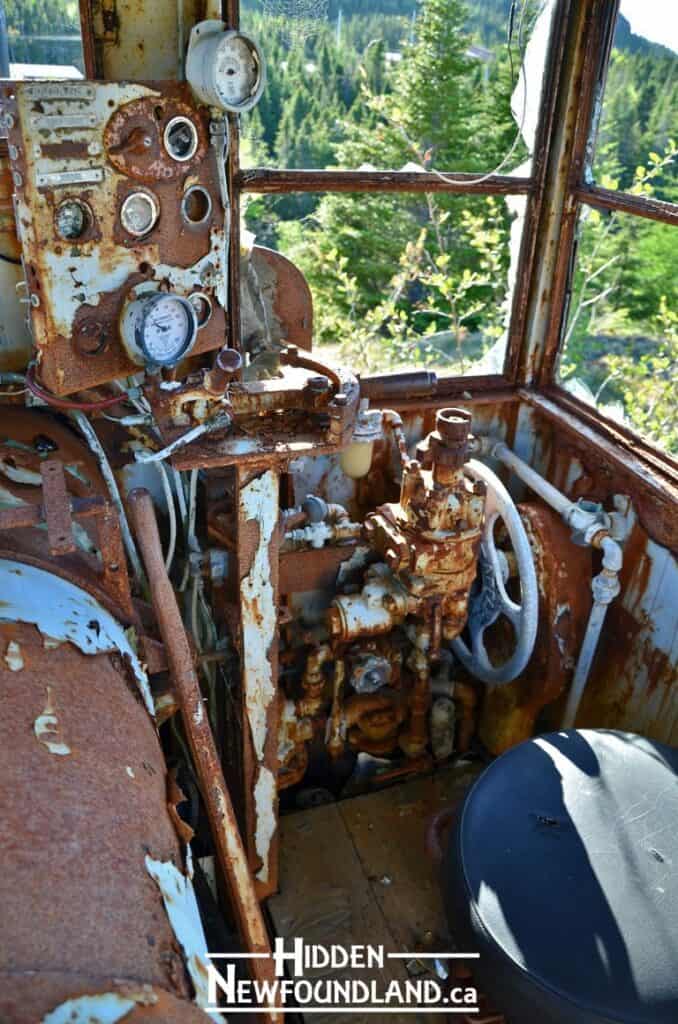 Rusty train cockpit with gauges and controls, surrounded by green forest views.