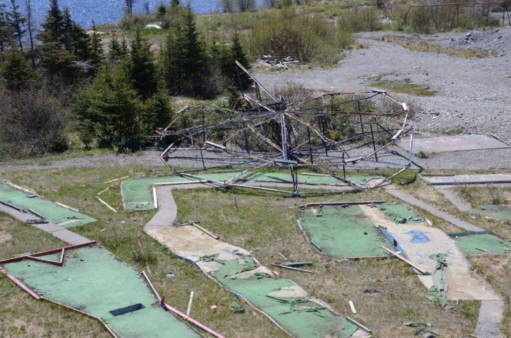 Ruined miniature golf course with broken structures and overgrown grass.