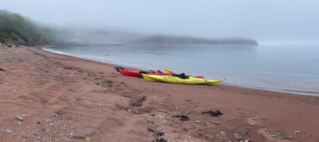 Yellow and red kayaks on a quiet beach with misty shoreline.
