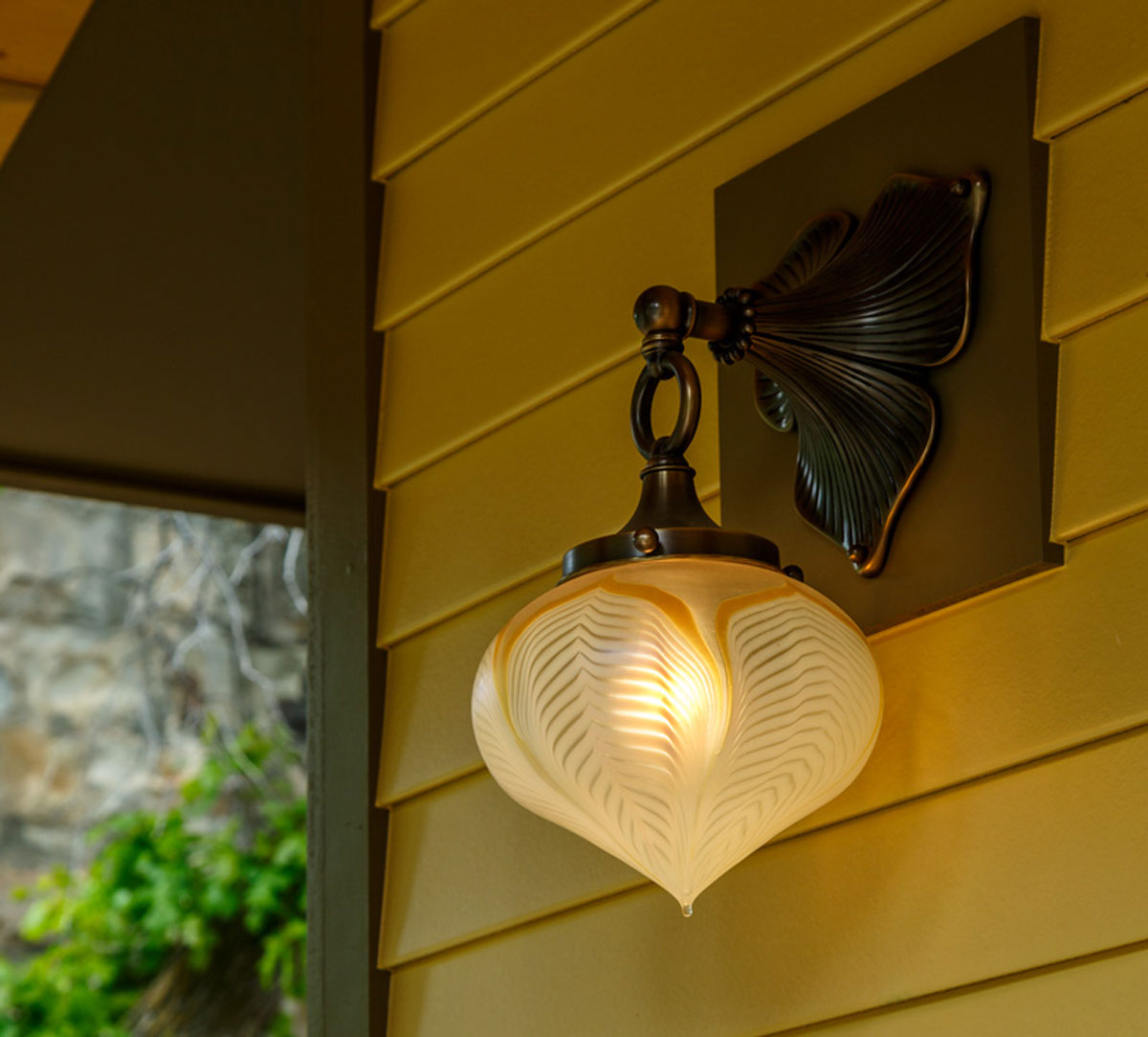 Vintage exterior wall sconce with leaf-shaped backplate on yellow siding.